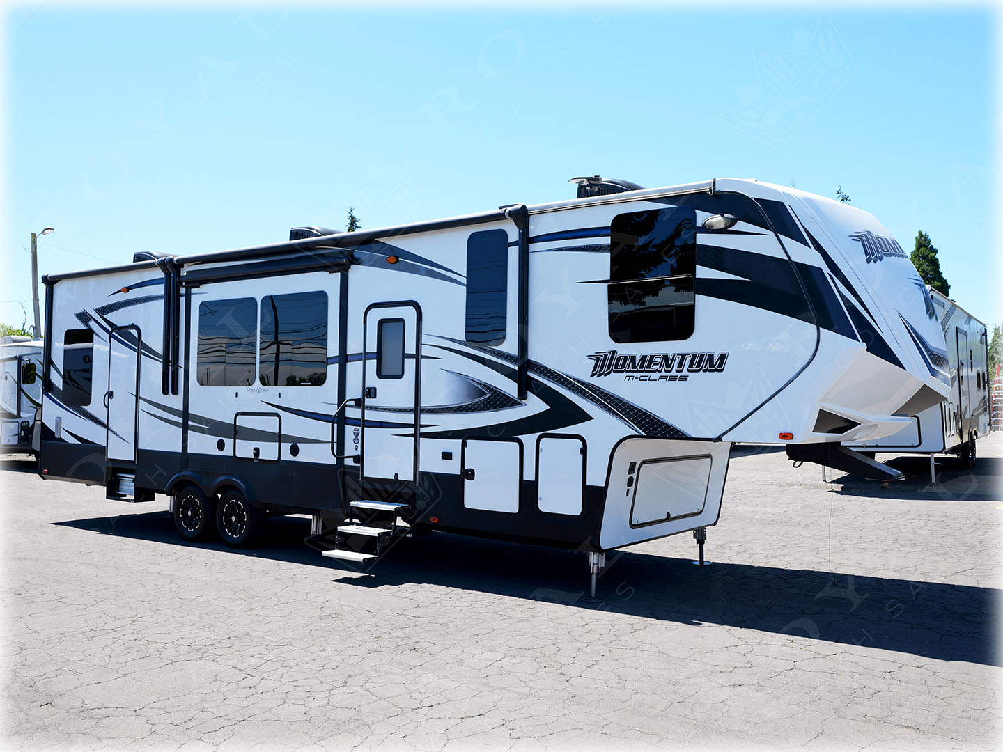 White and navy Momentum travel trailer with large slide-out room displayed at RV dealership