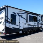 Side view of white and navy Momentum M-Class RV with extended slide-out awning and multiple windows displayed at dealership