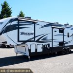 White and blue Momentum M-Class travel trailer RV parked in lot with extended awnings and dual axles
