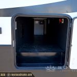 Open exterior storage compartment on white and blue RV showing empty black interior space