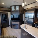 Spacious RV interior showing open floor plan with kitchen island, fireplace, entertainment system, and multiple storage cabinets