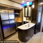 Modern RV kitchen with stainless steel appliances, white quartz countertop island with sink, dark wood cabinetry, and pendant lighting