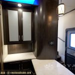 RV bathroom vanity area with dark wood cabinetry, white countertops, medicine cabinet, and entertainment unit