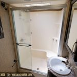 Modern RV bathroom with glass shower enclosure, white sink, and textured wall panels