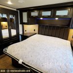 Spacious RV master bedroom with king bed, dark wood cabinetry, blue accent lighting, mirrored closet doors, and large windows