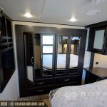 RV bedroom viewed from doorway showing queen bed, dark wood cabinetry with mirrored doors, window with water view, and side table