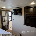 RV interior living area with TV mounted on wall, dark wood cabinetry, tan walls, and entrance door