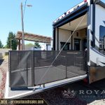 White travel trailer with extended black awning and mesh screen room at Royal Coach Sales lot