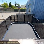 Open black enclosed cargo trailer bed with mesh sides and blue trim at storage facility
