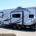 White and black Glacier Peak travel trailer with slide-out awning parked at Royal Coach Sales lot