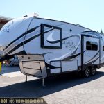 Exterior view of white Glacier Peak travel trailer RV with black graphics and extended slide-out on display lot