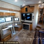 Full RV living space with dinette, kitchen area, wall-mounted TV, fireplace, black leather seating, and wooden decor