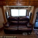 Spacious RV bedroom with burgundy leather reclining sofa, large windows with shades, wooden cabinetry, and carpeted floor