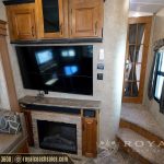 RV living room with fireplace, wall-mounted TV, wooden cabinetry, brown leather sofa, and hallway entrance