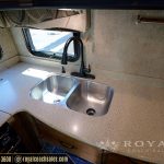 RV kitchen sink with dual stainless steel basins, black faucet, window above sink, beige countertops, and wooden cabinets