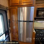RV kitchen with stainless steel refrigerator, black gas range stovetop, wooden cabinetry, microwave oven, and entrance door