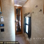 RV hallway interior showing beige fabric walls, wooden trim, black hooks for storage, window with curtains, and climate control thermostat