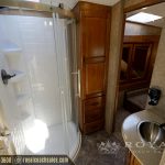 RV bathroom with walk-in shower with glass enclosure, white subway tile walls, wooden storage cabinet, and stainless steel sink
