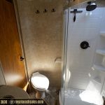 RV bathroom with toilet, wooden door, shower area with hooks for towels, and compact sink fixtures