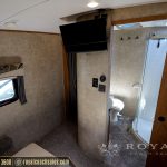 Interior bathroom and bedroom area of RV with TV mounted on wall, toilet, shower enclosure, and wood trim