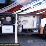 RV exterior storage compartments showing Aqua-Hot 450D water heater system and plumbing fixtures on white and red motorcoach