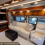 Spacious RV living room with cream leather sofa, recliner, fireplace, and flat-screen TV with wooden cabinetry