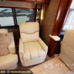 Cream-colored recliner chair in luxury RV living area with wooden cabinetry and windows