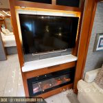 RV living area with flat-screen TV mounted above an electric fireplace insert, cream-colored leather seating, and wood frame details