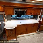 Spacious RV kitchen with curved white countertop, island seating, wood cabinetry, microwave, and panoramic window