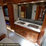 Elegant RV bathroom vanity with dual stainless steel sinks, wood cabinetry with drawers, striped tile backsplash, and large mirror