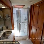 Modern RV master bathroom with large glass shower enclosure, dual round mirrors, wood cabinetry, and stainless steel sink