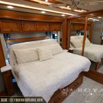 Luxury RV bedroom with two queen beds, cream bedding, wood cabinetry, overhead storage, and mirror accents