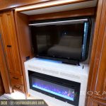 RV entertainment center with flat-screen TV mounted above electric fireplace with blue flame effect and wooden storage cabinets