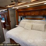 RV master bedroom featuring queen bed with cream bedding, mirrored closet doors, and wooden cabinetry throughout