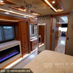 Luxury RV master bedroom with queen bed, electric fireplace, wood cabinetry, and modern lighting fixtures