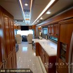 Interior hallway of luxury motorcoach with wooden cabinetry, kitchen area, and climate control vents