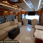 Spacious motorcoach living area featuring beige leather furniture, flat-screen TV, and ambient ceiling lights