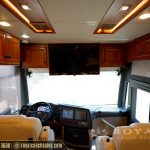 Open floor plan of luxury motorcoach interior with cream-colored seating, wooden cabinetry, and LED lighting